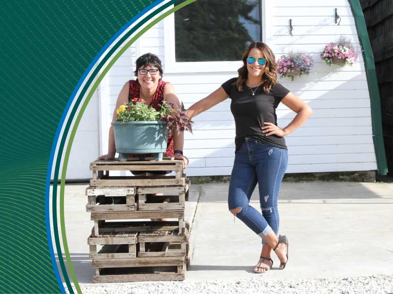 Two women smiling outdoors near a white house with flowers, promoting agricultural safety.