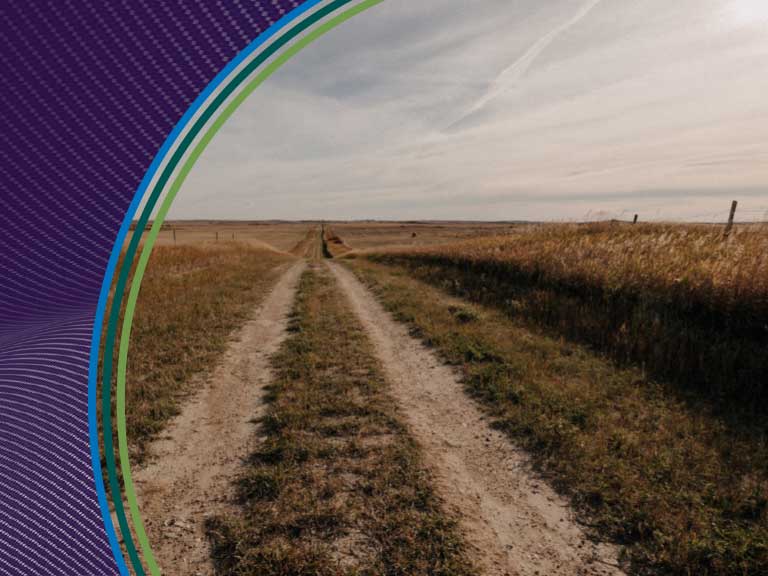 Rural dirt road in open farmland under cloudy sky, agricultural safety focus.