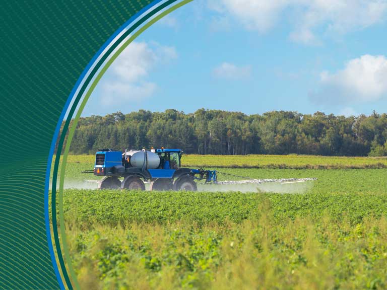 Sprayer applying pesticides in a green field on a sunny day.