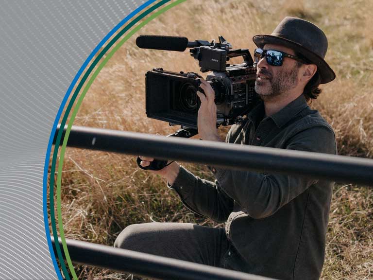 A man filming outdoors with professional camera equipment in a rural field.