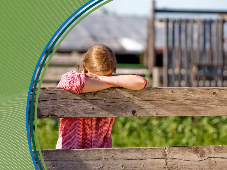 A woman leaning on a wooden fence on a farm, with a barn in the background.