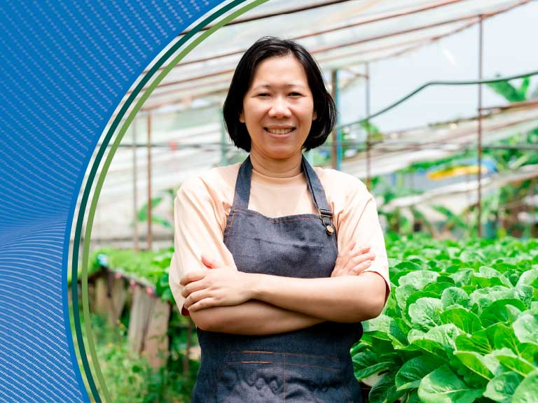 Healthy female farmer standing in a greenhouse with lush green leafy vegetables.