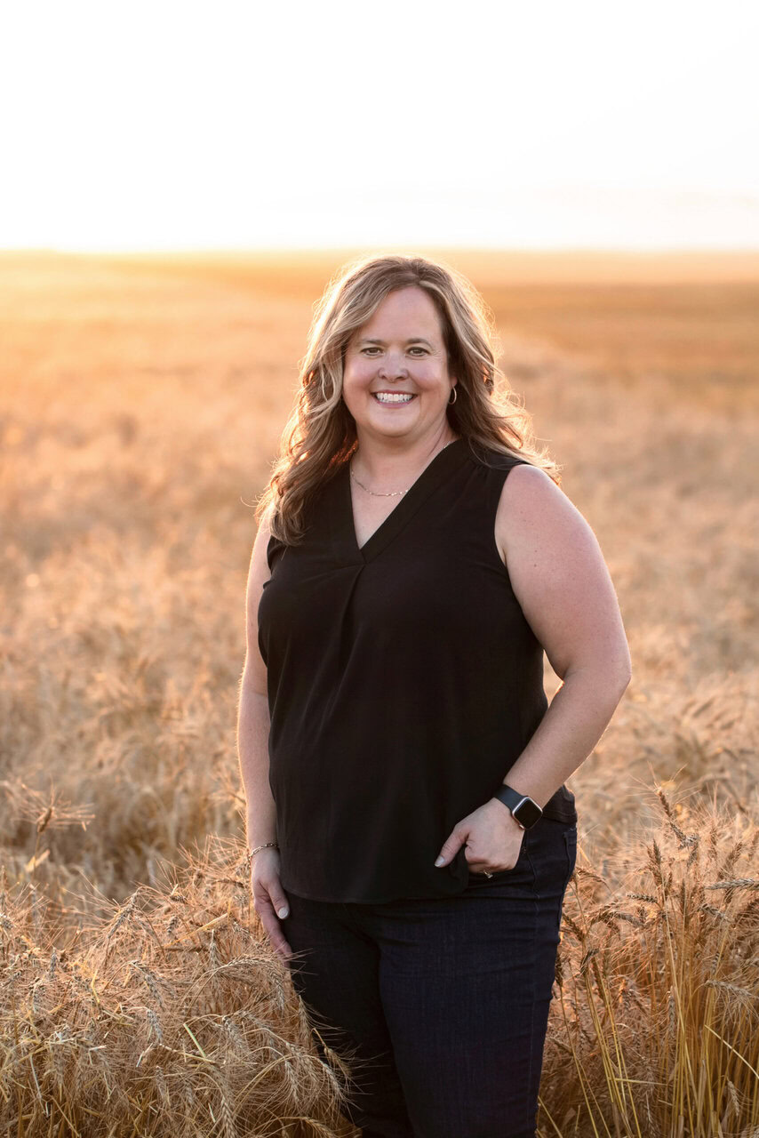 Smiling woman standing in a wheat field at sunset, representing agricultural safety.